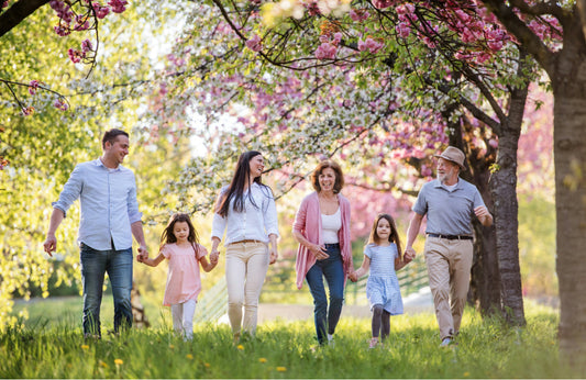 Mehrgenerationen-Familie spaziert im Frühling unter blühenden Kirschbäumen – Symbol für natürliche Pflege in jedem Lebensalter.